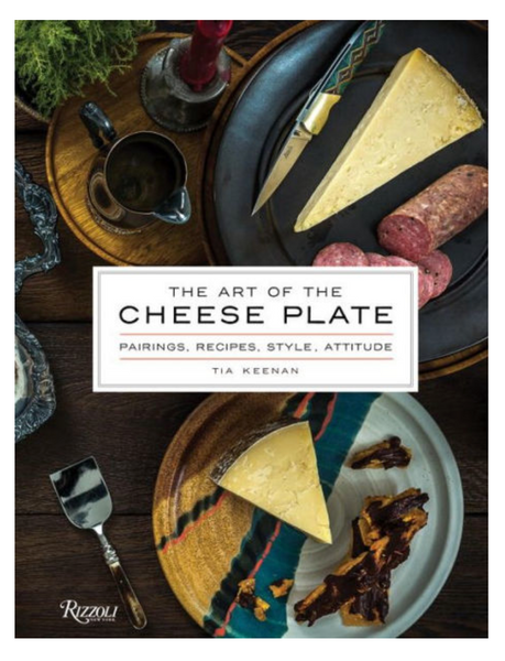 The Rizzoli book "The Art of the Cheese Plate" by Tia Keenan showcases elegantly arranged cheese pairings, salami, and condiments on plates with utensils, exuding entertaining elegance.