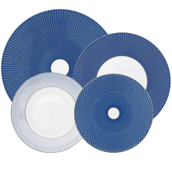 Four blue and white patterned plates of varying sizes are arranged with overlapping edges. The Raynaud Tresor Blue Collection plates boast intricate detail with a circular, textured design, showcasing the elegance of hand-painted poetic porcelain from Raynaud.