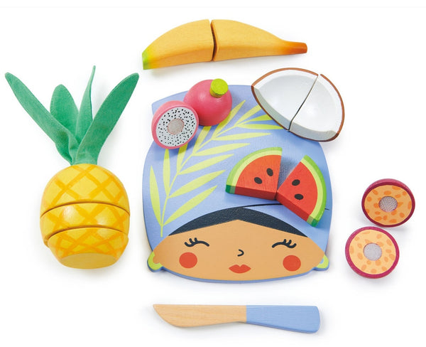 The Tenderleaf Tropical Fruit Chopping Board by Tender Leaf Toys is a delightful toddler kitchen toy that features a wooden cutting board surrounded by charming wooden fruits such as banana, coconut, dragon fruit, watermelon, pineapples, and passionfruit slices—all accompanied by an adorable wooden knife.