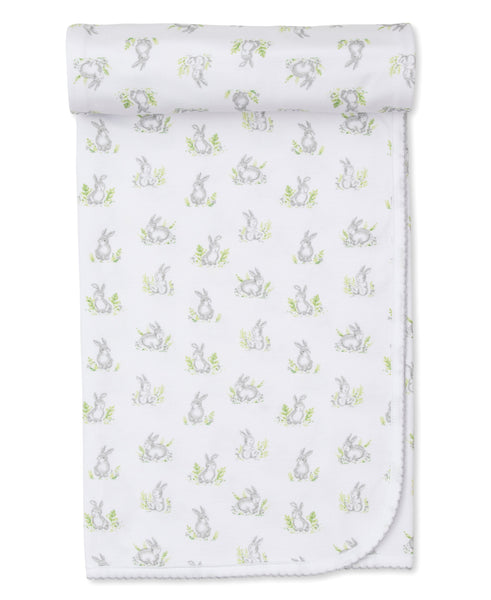 The Kissy Kissy Cottontail Hollows Blanket by Kissy Kissy is a rolled-up white baby blanket adorned with light grey bunnies and green foliage, crafted from soft Pima cotton.