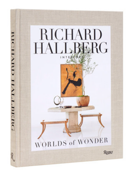 A beige cover of a book titled "Worlds of Wonder," featuring a minimalist table with decor items, including a potted plant and an artwork. Showcasing the modernity brought by Los Angeles interior designer Richard Hallberg, this book is published by Rizzoli.