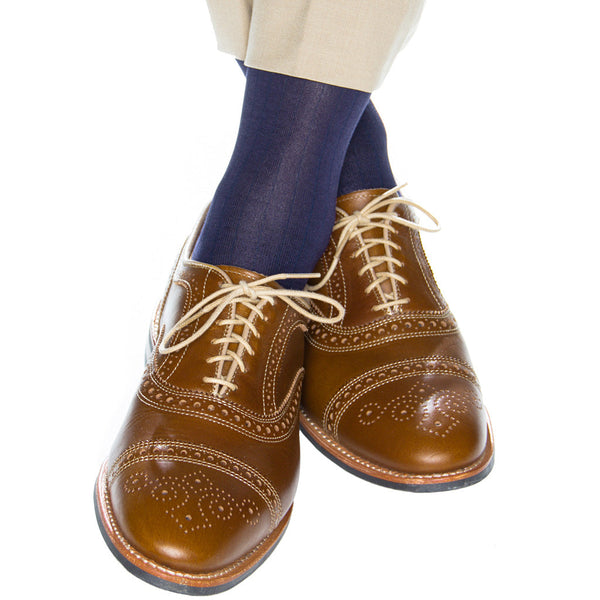 A person wearing beige pants, Classic Navy Dapper Classics Ribbed Mid Calf Socks, and brown brogue leather shoes with white laces. The shoes and socks are in focus, showcasing the elegance of the breathable material.