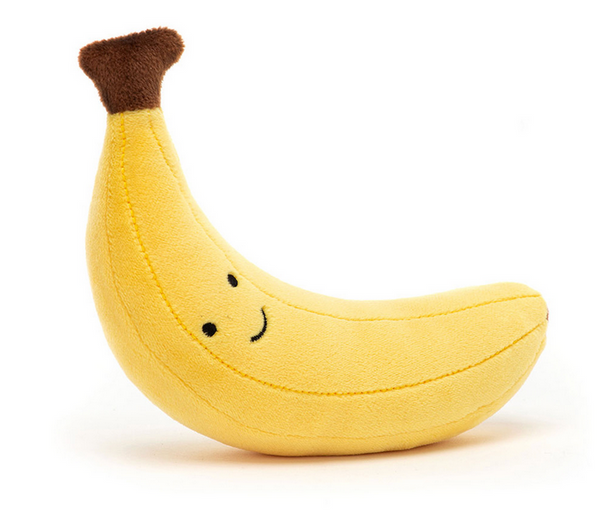 A Jellycat Fabulous Fruit Banana with a smiling face and brown tip, made from stretchy fur and polyester fibers, positioned at an angle, isolated on a white background.