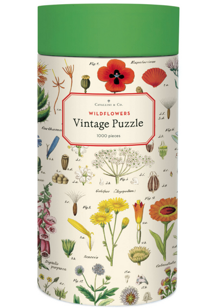 A cylindrical box containing the 1,000-piece Cavallini & Co. Wildflowers Puzzle by Cavallini Papers and Co., featuring illustrations of various flowers and plants, comes with a handsewn muslin bag for easy storage.