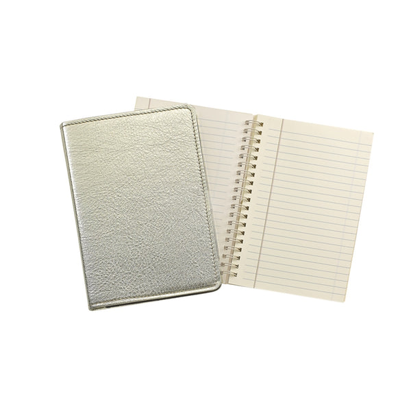 A Graphic Image Leather Wire Ring Notebook in white gold lies gracefully next to an open spiral-bound notebook with lined pages, making it the ideal companion for any writer.