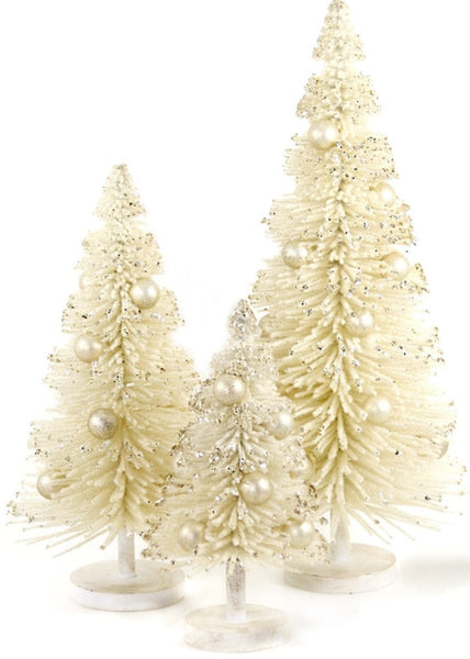 A large 15-inch Cody Foster Snow Laden Tree stands among three decorative white Christmas trees, adorned with glitter and pearl-like ornaments. The graceful creation from Cody Foster adds elegance to the display with its pristine white base.