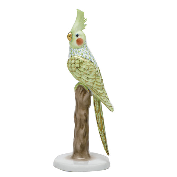 A hand-painted Herend Cockatiel in Key Lime Green, perched on a brown tree stump, isolated on a white background.