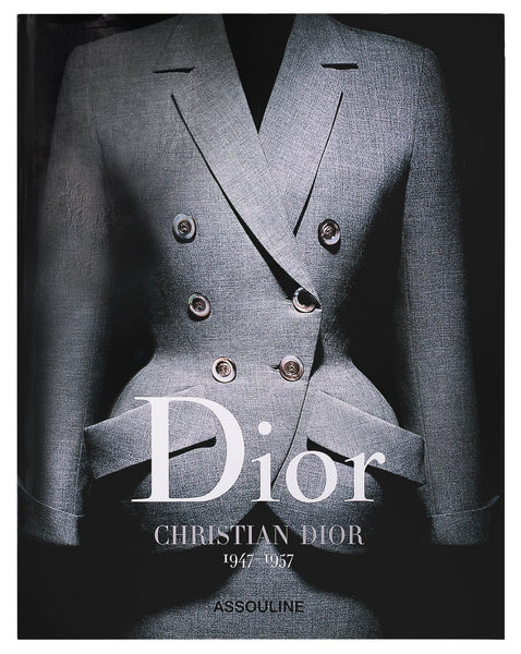 The image shows the cover of a book titled "Dior I by Christian Dior" published by Assouline. Showcasing one of Dior's haute couture designs, the cover features a gray double-breasted suit with prominent buttons.