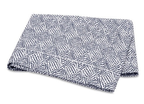 A folded, navy blanket from the Matouk Duma Diamond Bedding Collection, featuring a geometric design with a 500 thread count, lies on a white background.