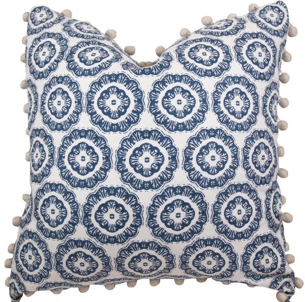 A handmade 22" x 22" pillow featuring a white background and a repeating blue circular pattern, adorned with beige pom-poms along the edges, the Tassel Inverted Medallion Navy Pillow by Associated Design.