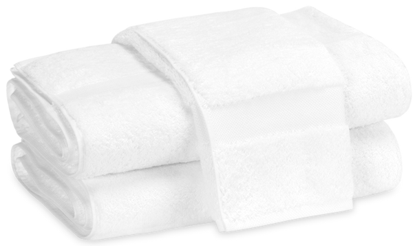 Two neatly folded towels from the Matouk Lotus Bath Collection - White, stacked on top of each other and bound by a white band.