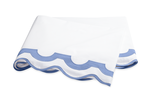 Folded white fabric with a scalloped blue trim along the edges, made from luxurious Egyptian cotton percale from the Matouk Mirasol Bedding Collection, Azure by Matouk.