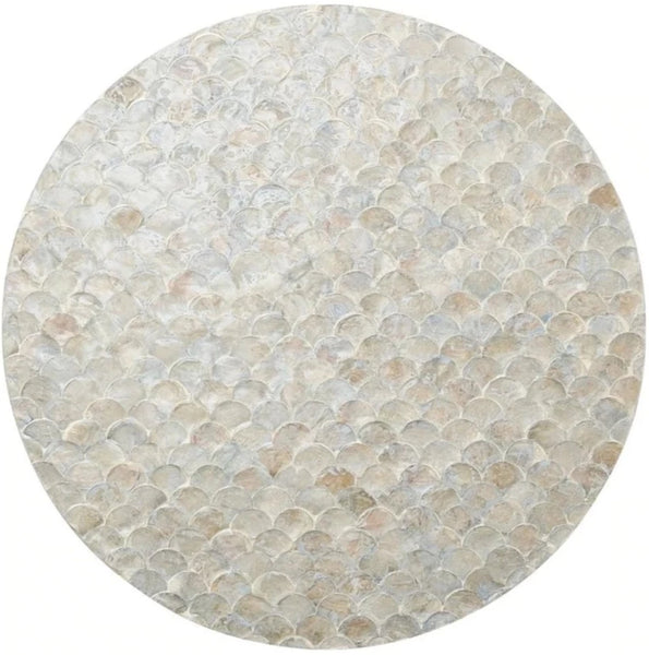 A circular stone mosaic tile featuring an overlapping scale-like pattern in various shades of white and grey, reminiscent of a Kim Seybert Camellia Placemat, Gray. This unique design is enhanced by the delicate, hand-dyed Capiz shells that add a touch of elegance.