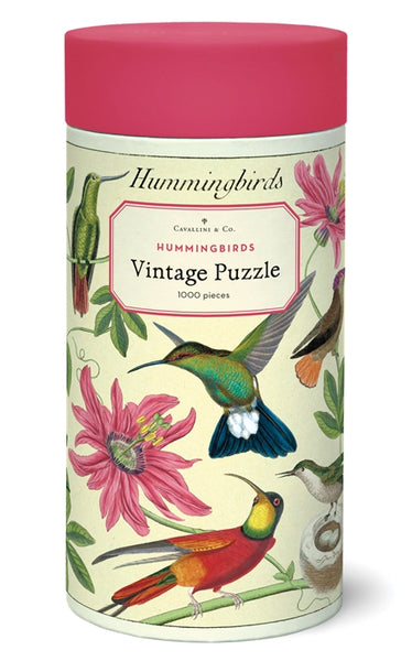 A cylindrical box titled "Cavallini & Co. Hummingbirds 1,000 Piece Puzzle" by Cavallini Papers and Co, decorated with vibrant illustrations of hummingbirds and pink flowers. Contains 1000 pieces.