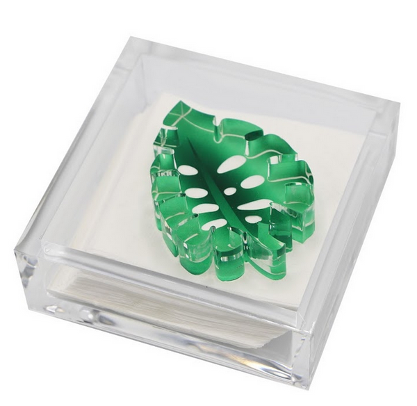 An Tara Wilson Designs acrylic box with a green leaf, perfect as a hostess gift or Tara Wilson Designs Cocktail Napkin Holder with Monstera Leaf Weight.