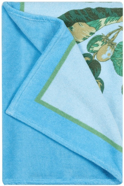 Introducing the Matouk Tallulah Palm Beach Towel in Peacock Green: a luxurious light blue cotton terry creation featuring green and yellow tropical leaf and fruit patterns on one corner, accented elegantly with a green border detail. This summer essential from Matouk is perfect for adding a touch of tropical elegance to your beach outings.