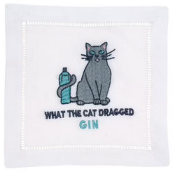 An elegant August Morgan Cocktail Napkins What The Cat Dragged Gin, Set of 4 featuring a white fabric square, embroidered with a gray cat sitting next to a bottle, and the text "WHAT THE CAT DRAGGED" in black and "GIN" in blue. Perfect for adding a touch of humor to any gathering.