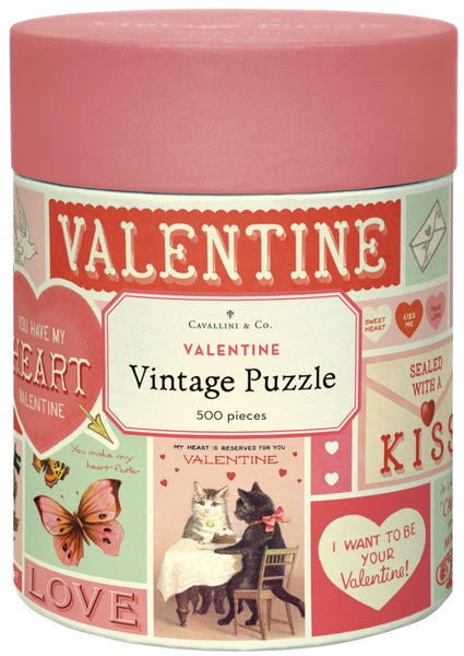 A cylindrical box featuring the Cavallini Valentine 500 Piece Puzzle by Cavallini Papers and Co, embellished with romantic illustrations such as cats, butterflies, and hearts. This puzzle comes stored in an enchanting handsewn muslin bag and is inspired by the timeless charm of the Cavallini archives.