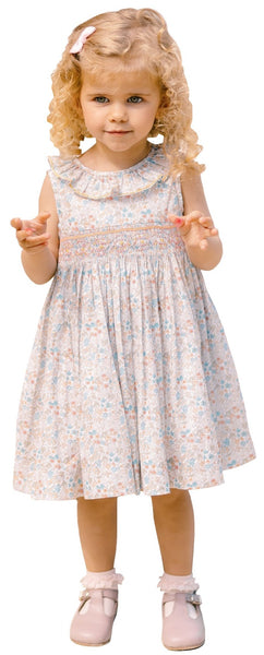 A young girl with curly blonde hair, wearing the Antoinette Girls' Angele Dress made of 100% poplin cotton and pink shoes, stands with her hands up.