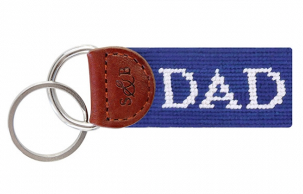 A Smathers & Branson Dad Key Fob with the word "DAD" embroidered in white on a blue fabric strap, attached to a brown leather loop with a metal key ring. This charming accessory, perfect for your pocket or purse, showcases both durability and a touch of colorful personality.