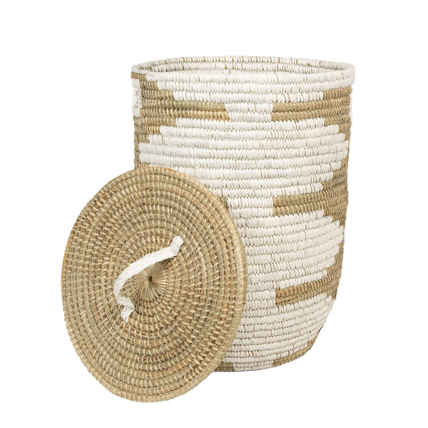 The Pigeon & Poodle Jelsa Round Hamper Natural/White Raffia, a woven hamper with a lid, features an intricate pattern of white and natural tan colors. The lid is seen leaning against the basket.