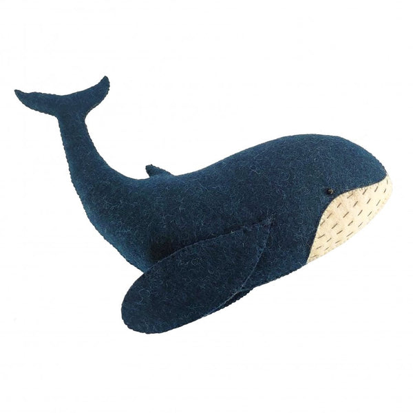 The Fiona Walker Whale Wall Decoration - Mini by Fiona Walker is a handcrafted plush toy shaped like a blue whale, featuring a dark blue body and light-colored underside. Made from organic wool with simple stitched details for the eyes and mouth, it is perfect for any nautical-themed room.