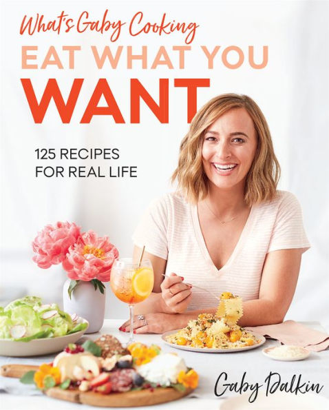 A smiling woman seated at a table with various dishes graces the cover of the Common Ground cookbook "What’s Gaby Cooking: Eat What You Want" by Gaby Dalkin, celebrating balanced eating with 125 recipes for real life.