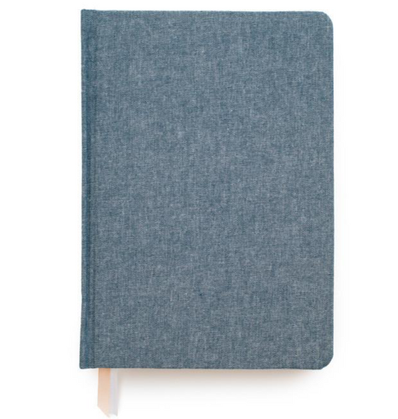 A closed Sugar Paper Tailored Chambray Journal from the brand Sugar Paper, featuring a blue chambray bookcloth cover, lined pages, and a ribbon bookmark peeking out from the bottom.