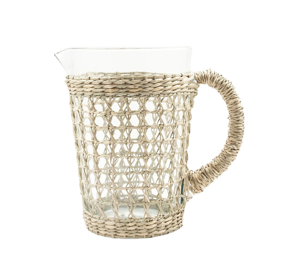 The Seagrass Wrapped Cage Pitcher by Be Home is an elegant glass pitcher with a woven rattan cover, ideal for both indoor and outdoor dining, and features a handle crafted from the same material.