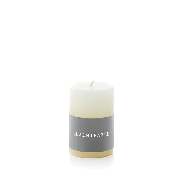 A Simon Pearce Ivory Pillar Candle, 2" x 3" with a grey and gold label that reads "Simon Pearce" on a white background.