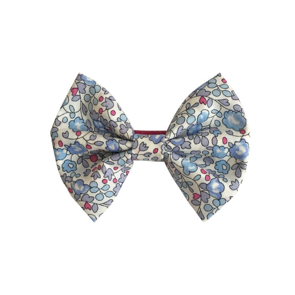 A small bow clip by Milledeux featuring a floral pattern with blue and pink flowers on a white background, made from exquisite Liberty Eloise D fabric.