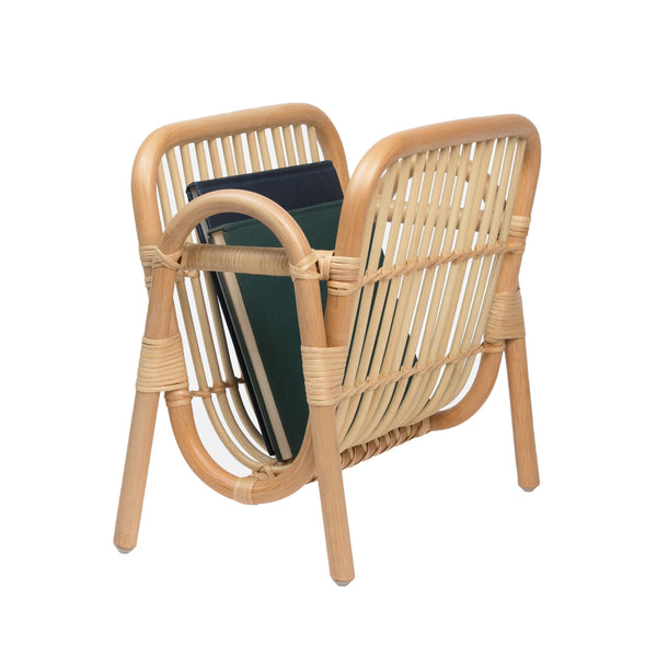 The Pigeon & Poodle Makassar Magazine Holder, designed by Pigeon & Poodle, is a naturally curved rattan magazine holder displaying several magazines and books with a sophisticated woven pattern, making it ideal for home decor.