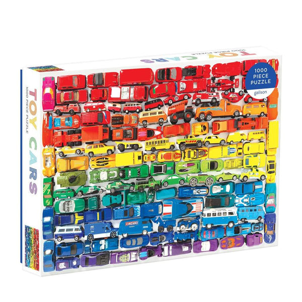 The Rainbow Toy Cars 1000 Piece Puzzle by Chronicle Books is a jigsaw featuring tightly arranged miniature toy cars in a stunning gradient layout, transitioning from red to purple shades. The title reads "Toy Cars.