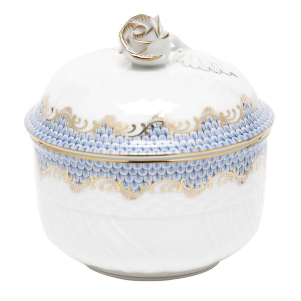 A finely crafted light blue porcelain container with a lid, adorned with intricate blue and gold fish scale detailing and boasting a rose-shaped handle on top. This exquisite piece is hand painted, showcasing the renowned craftsmanship of Herend's Fish Scale Serving Pieces collection.